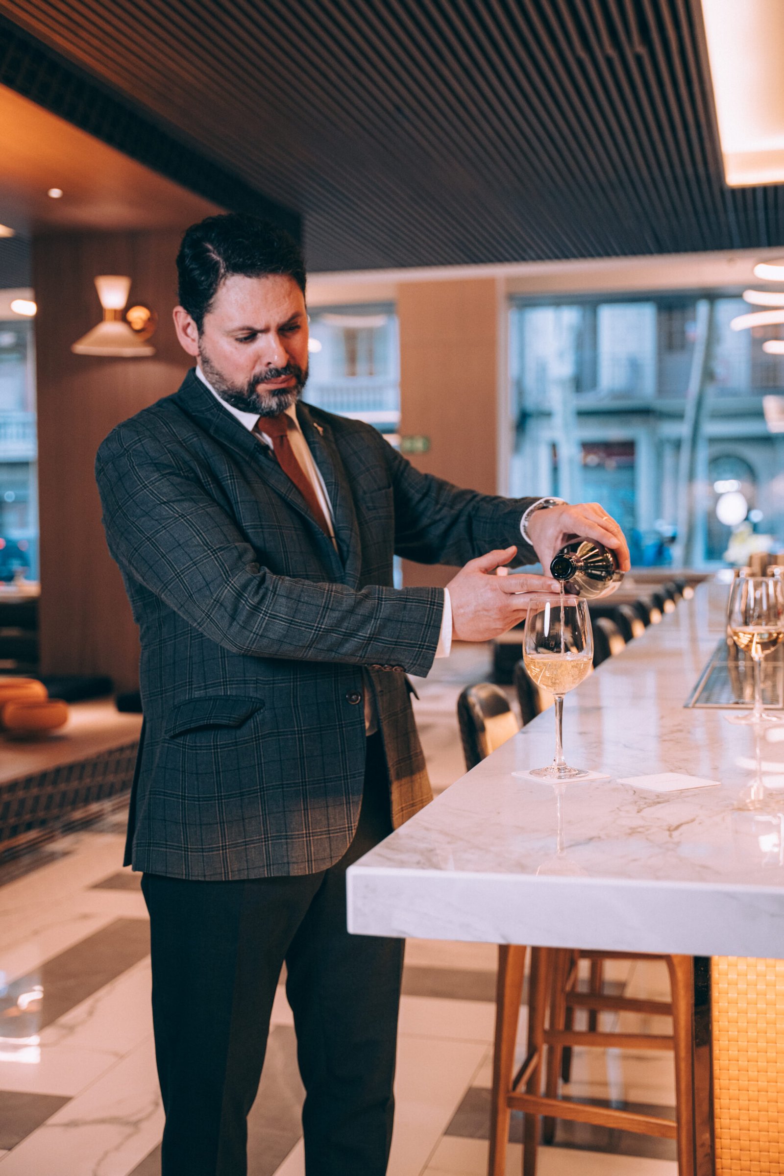 A person pouring a drink into a stemmed glass at a counter.